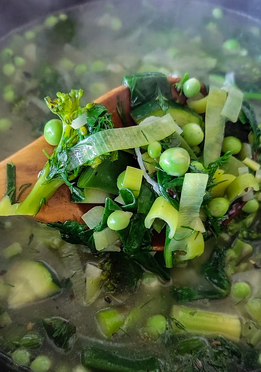 Stirring a pot of Spring vegetables in broth. The vegetables are leeks, peas, broccoli, zucchini and asparagus