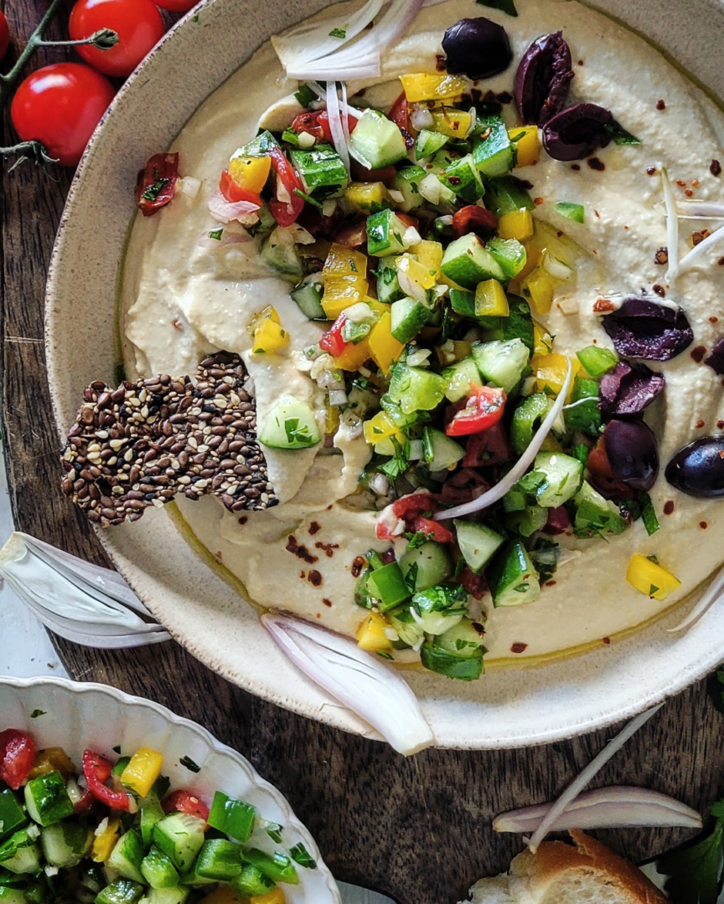 Bowl of creamy hummus covered with chopped cucumbers, peppers, onions, tomatoes and olives