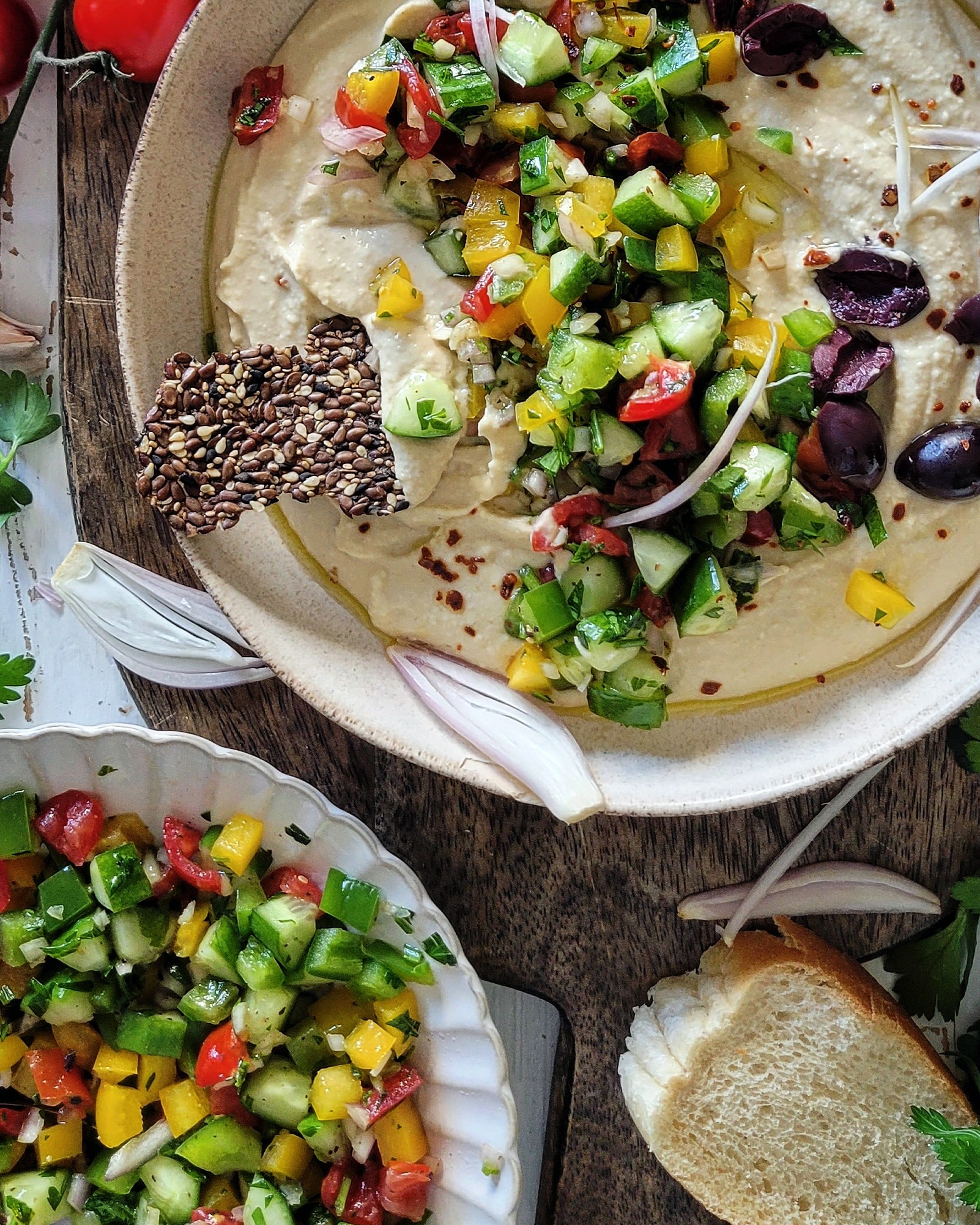 Bowl of creamy hummus covered with chopped cucumbers, peppers, onions, tomatoes and olives