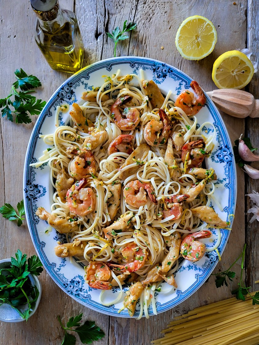 A large platter filled with pasta, shrimp and chicken in a garlic, butter and lemon scampi sauce