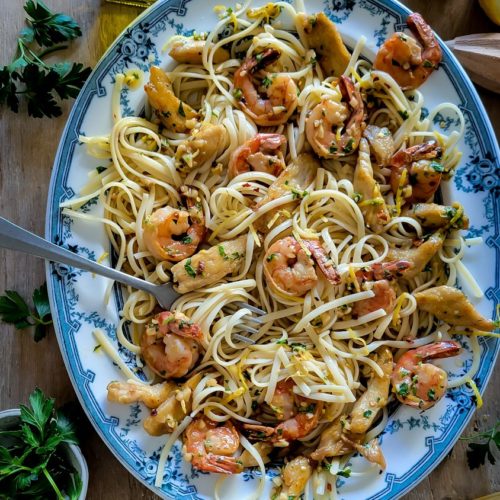 A large platter filled with pasta, shrimp and chicken in a garlic, butter and lemon scampi sauce