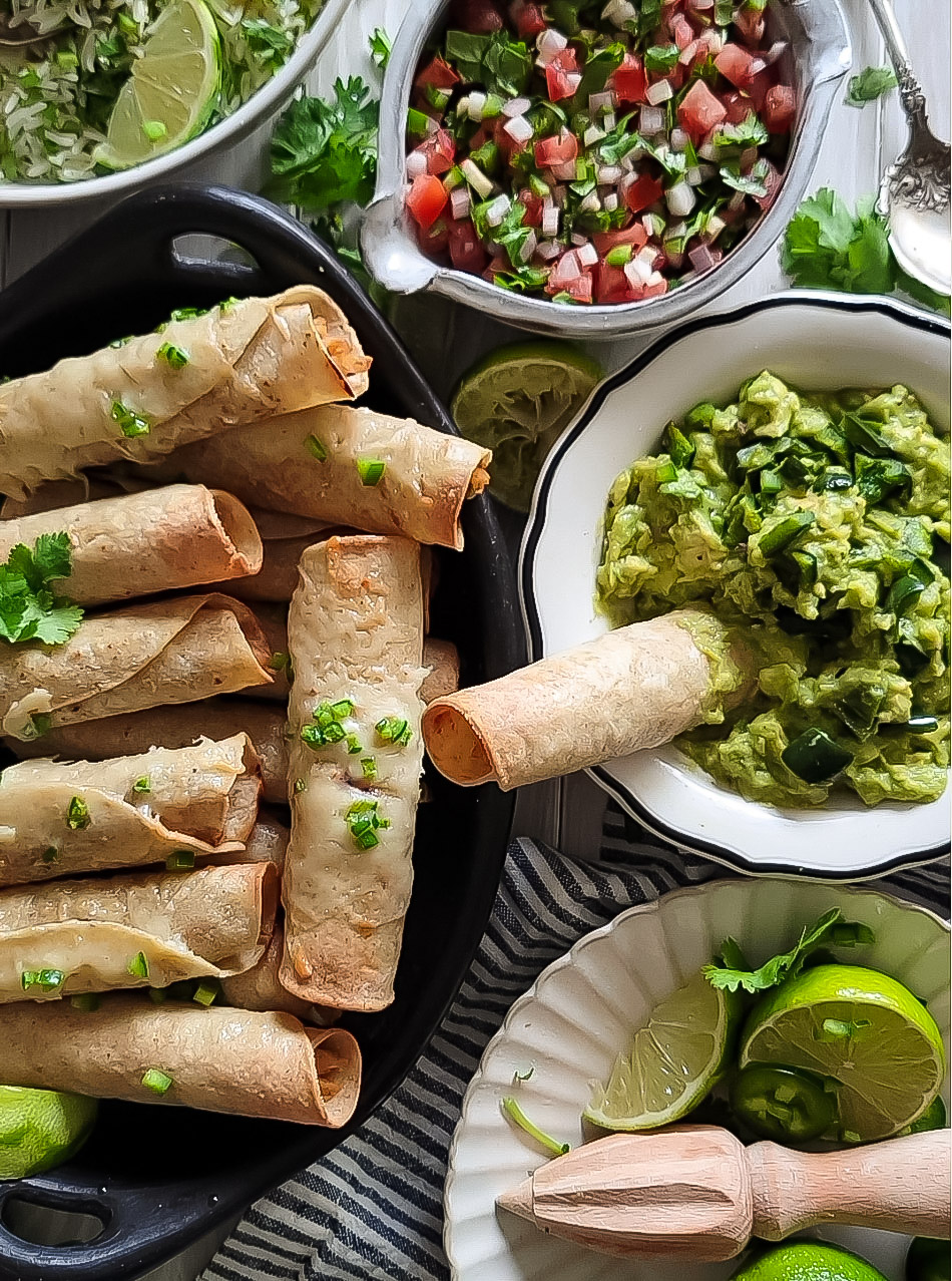 a table spread with chicken taquitos, pico de gallo, cilantro lime rice, and poblano guacamole