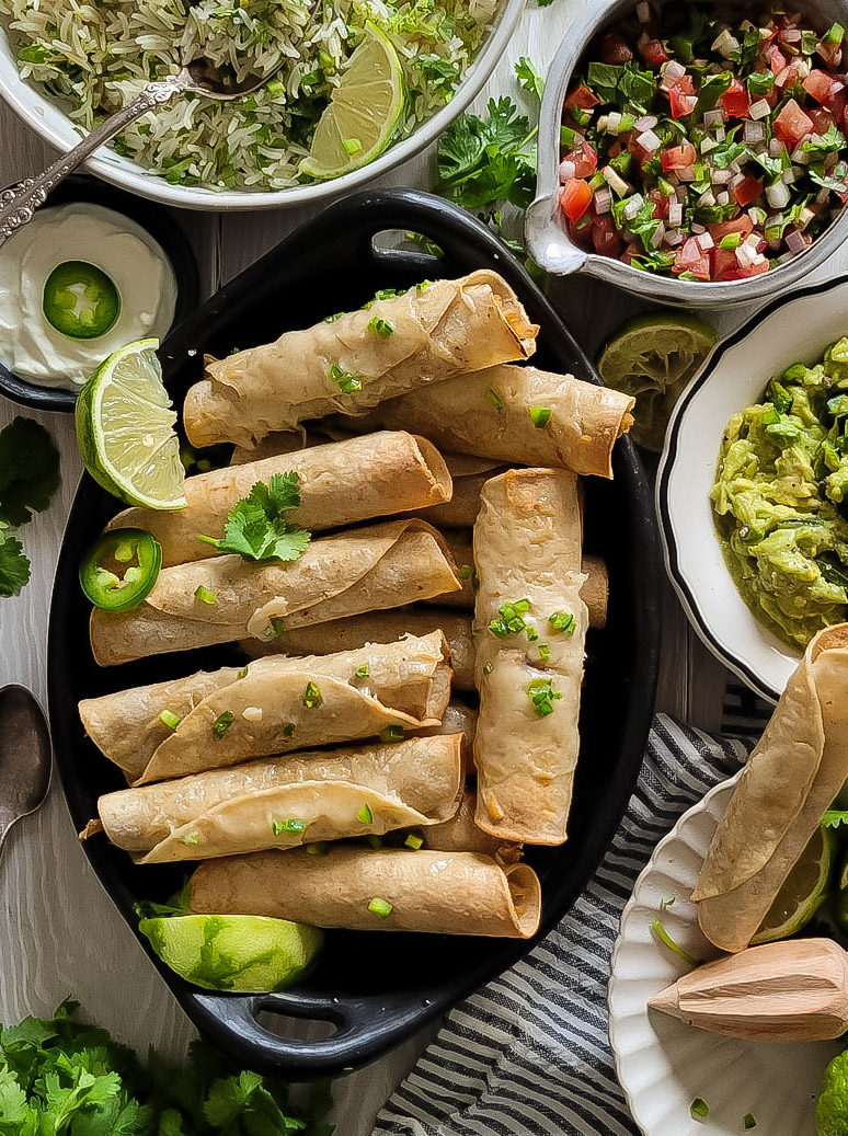 Chicken Taquitos on a platter served with cilantro lime rice, pico de gallo and poblano guacamole.