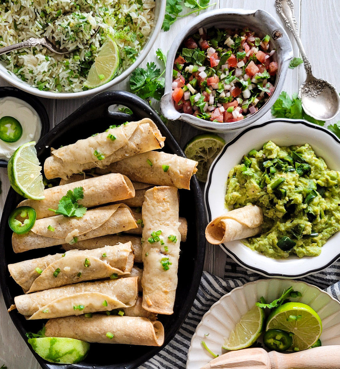 A mexican feast of chicken taquitos, cilantro lime rice, pico de gallo and poblano guacamole, limes and zester on a plate to the side