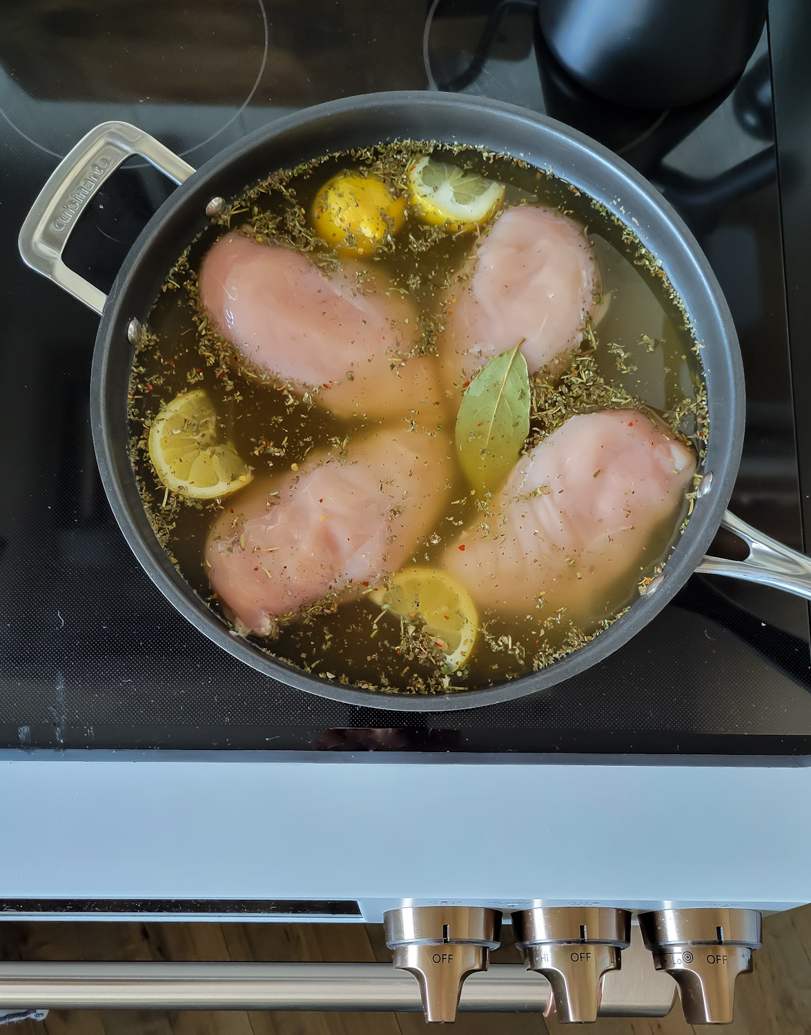 a pan filled with stock and chicken breasts being poached on the stove top