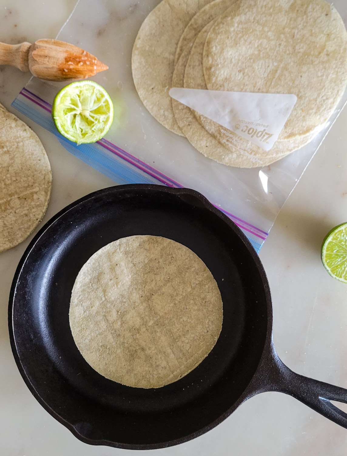cast iron pan with a corn tortilla, and a freezer bag of heated tortillas steaming inside to stay pliable.