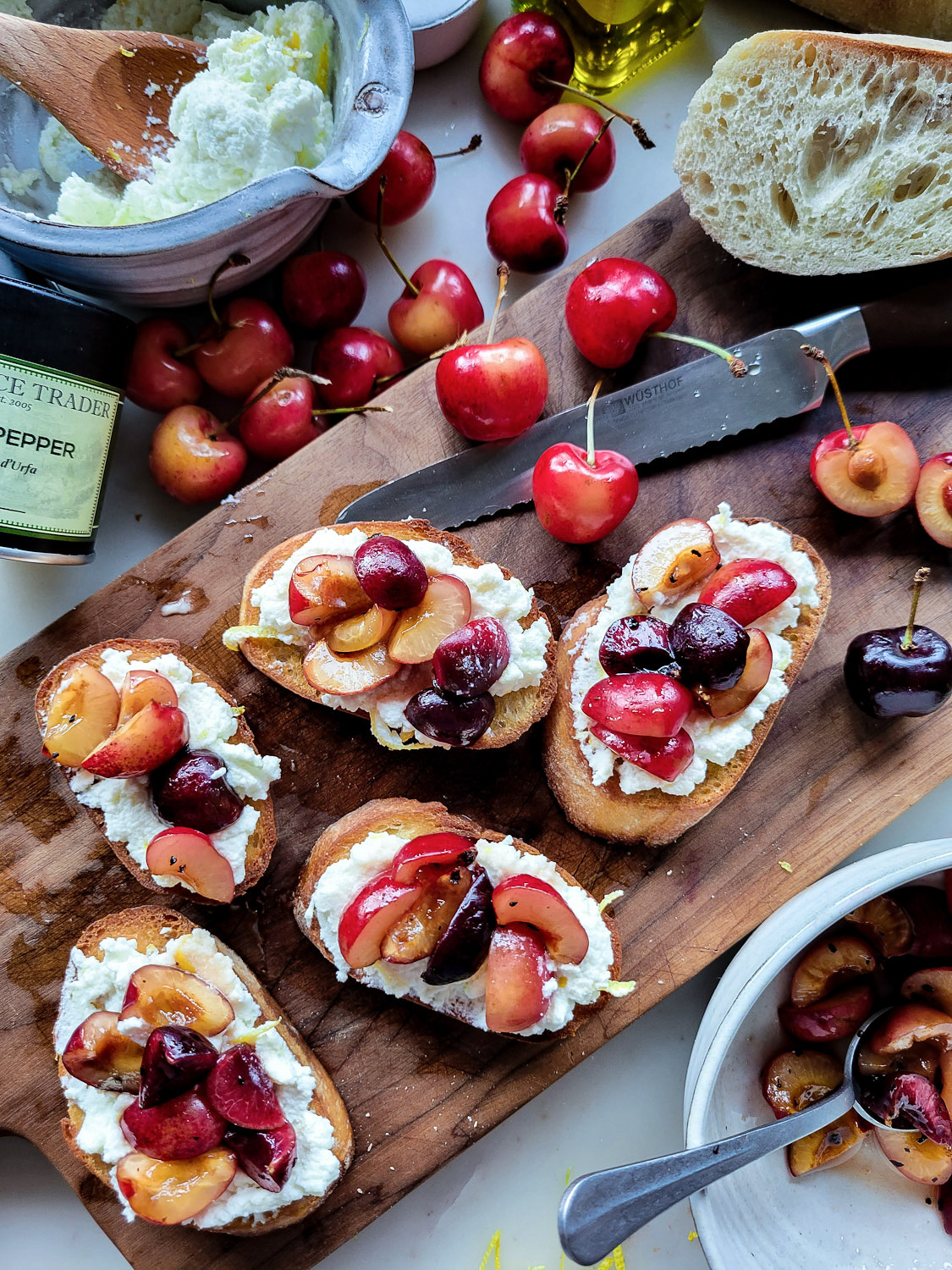a wooden cutting board with toasted crostini slices spread with lemon ricotta cheese and topped with chopped macerated cherries