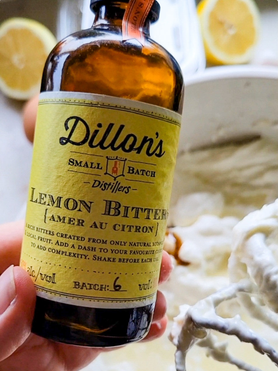 a bottle of lemon bitters with lemon cheesecake batter in a bowl in the background.