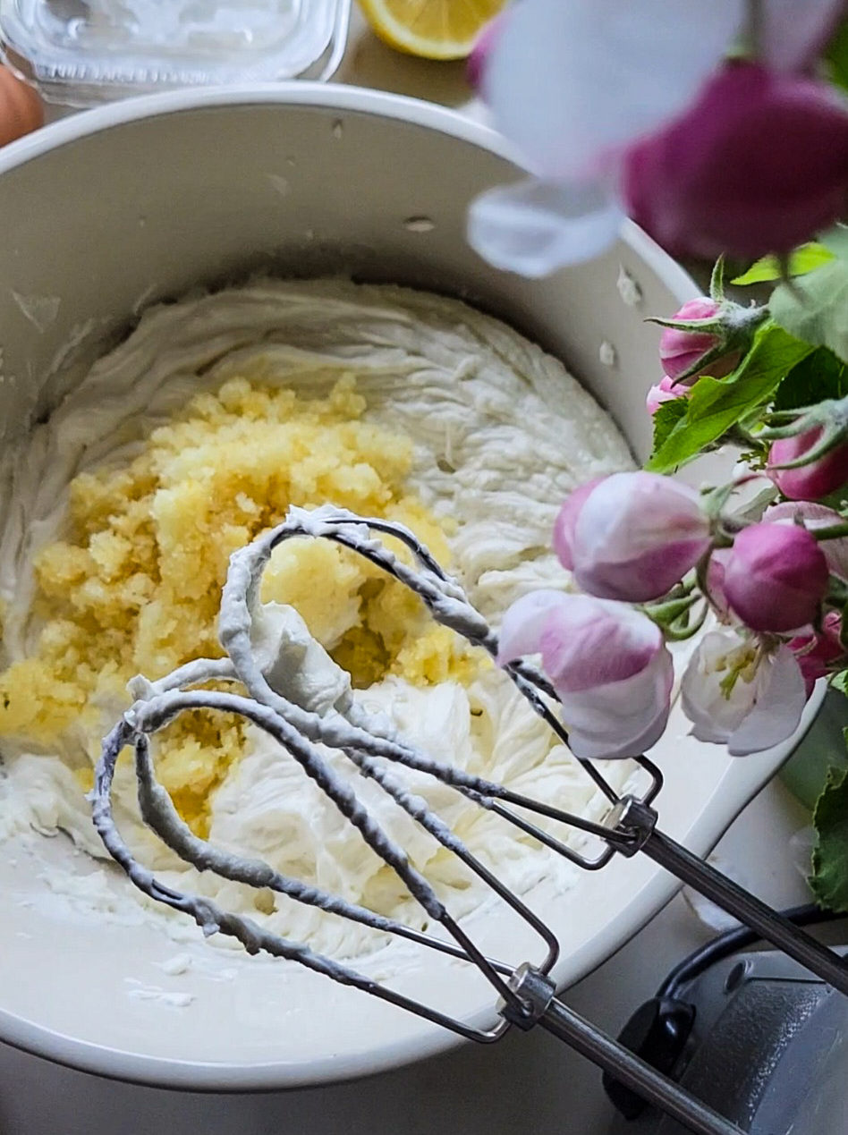 Lemon cheesecake batter in a bowl with lemon sugar sitting on top, the beaters of a handheld mixer in the foreground