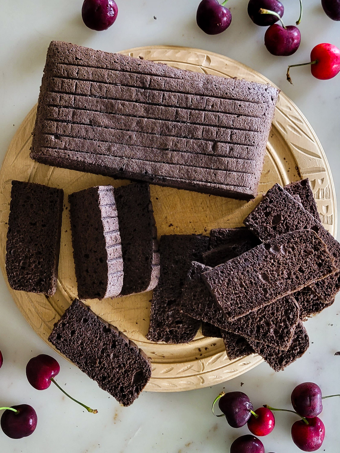 Baked chocolate sponge cake for black forest tiramisu, sliced on a wooden cutting board, and surrounded by fresh cherries.