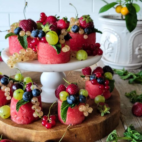 Tiered stand with watermelon cupcakes, sliced watermelon covered with fresh berries.