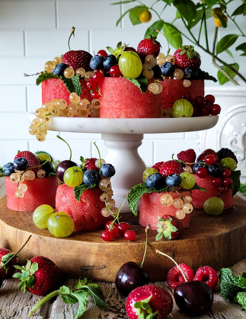 Tiered stand with watermelon cupcakes, sliced watermelon covered with fresh berries.