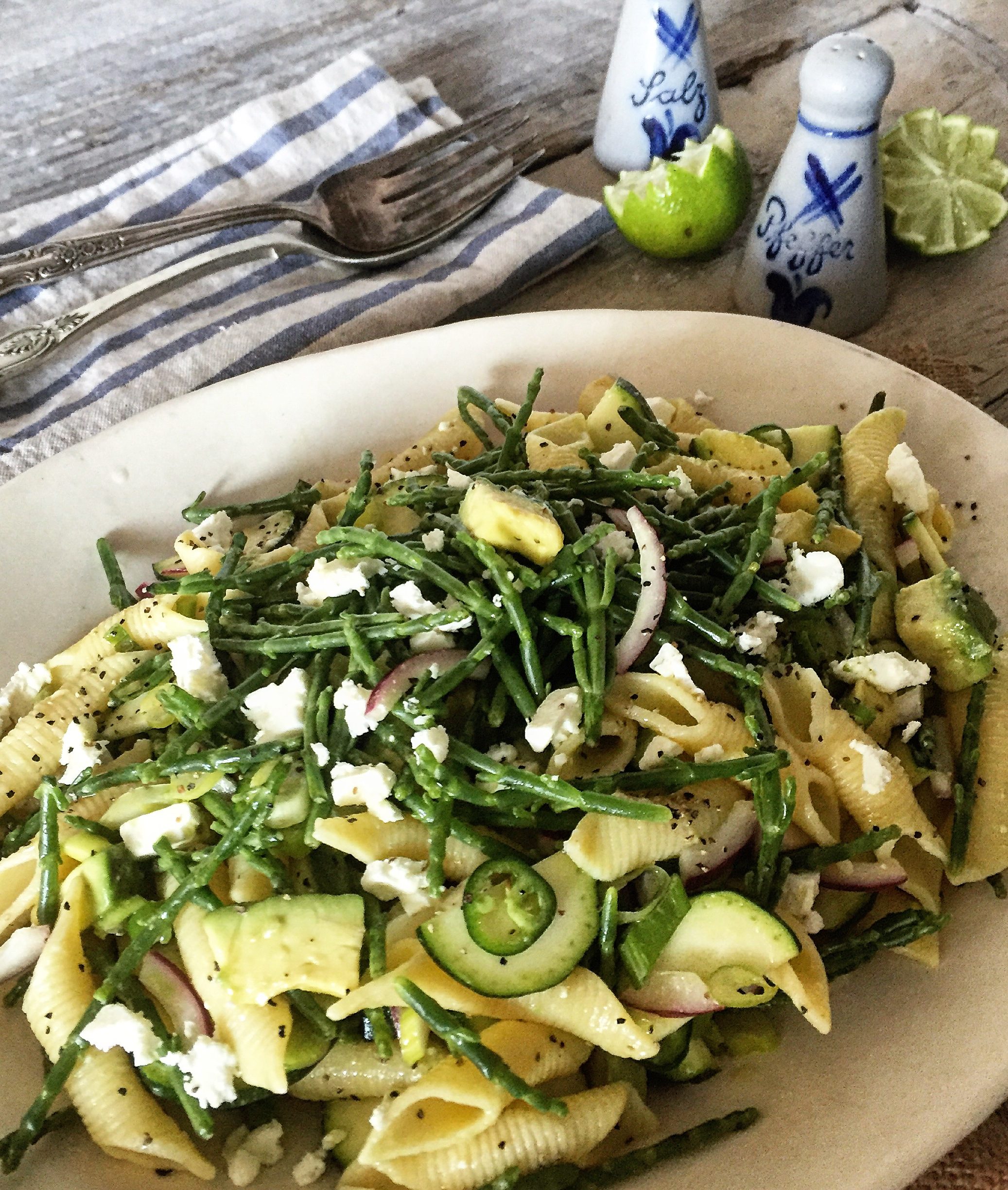 Platter with a Zuccchini and Sea Asparagus Pasta Salad, salt and pepper shakers and lime wedges in the background.