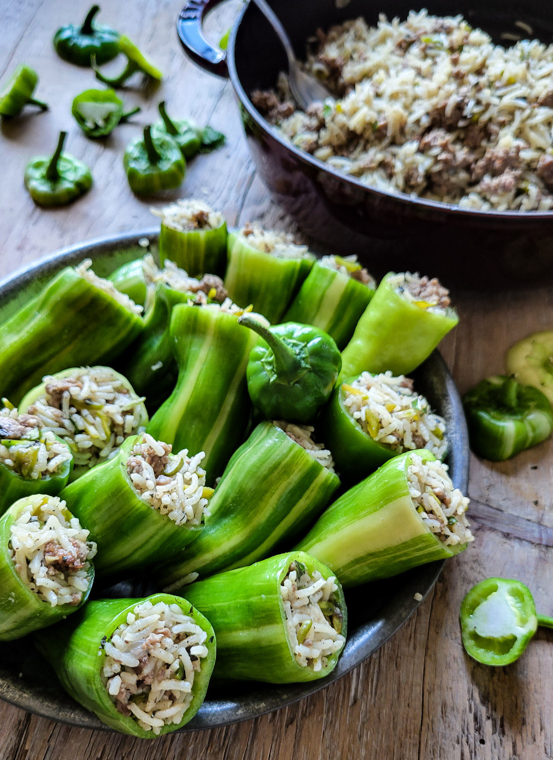 A pot of lamb and rice stuffing is to the side of a plate with freshly filled mini peppers.