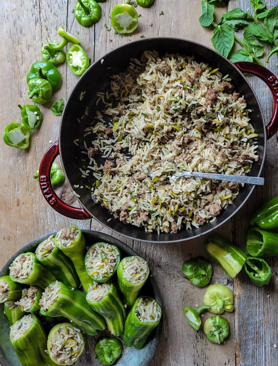 A pot of lamb and rice filling with a plate of stuffed mini peppers in front of it. Mint leaves and the tops of the peppers are scattered about.