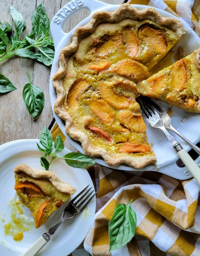 Peach Sour Cream Pie in a Basil Crust, a slice on a plate next to the pie with basil leaves surrounding everything.
