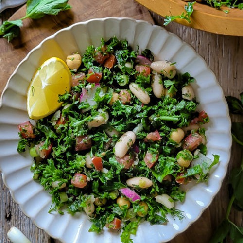 Close up of parsley and herb Tabouleh White Bean salad with a lemon wedge and mint leaves on the side.