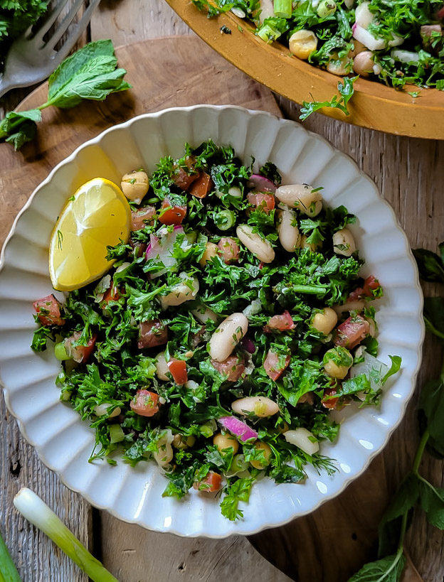 Close up of parsley and herb Tabouleh White Bean salad with a lemon wedge and mint leaves on the side.