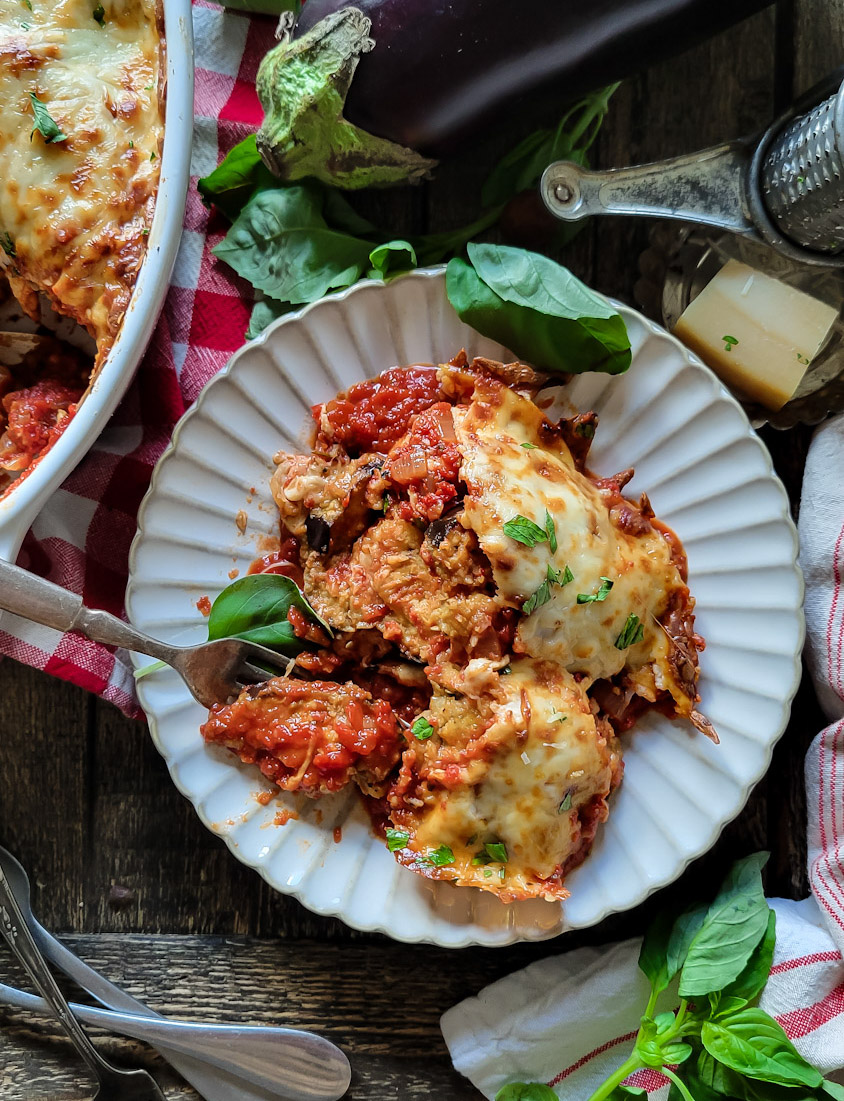 Serving of Lighter Eggplant Parmesan on a plate with basil leaves surrounding it.