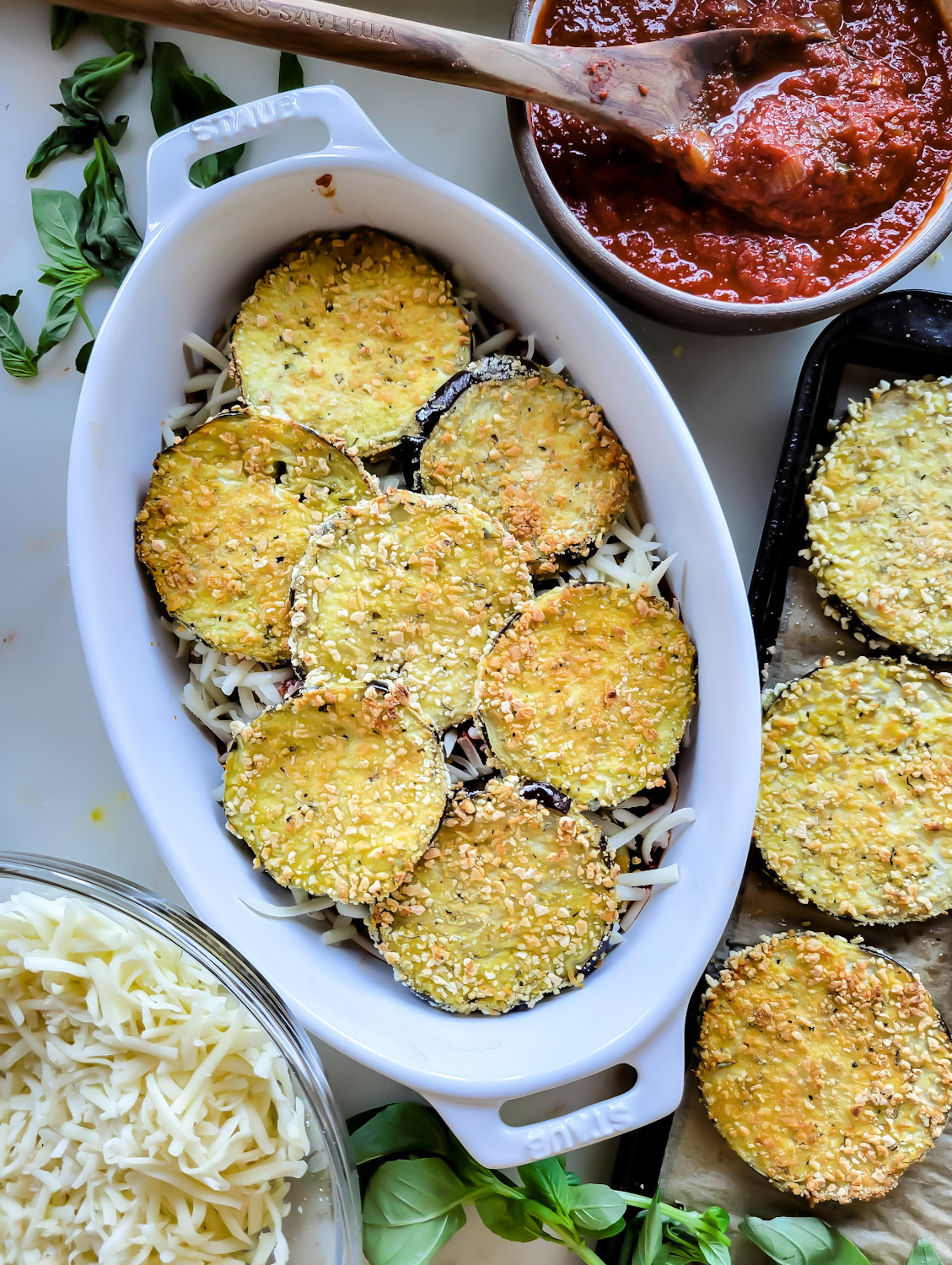 Prep shot of eggplant slices over cheese in a baking dish for Lighter Eggplant Parmesan.