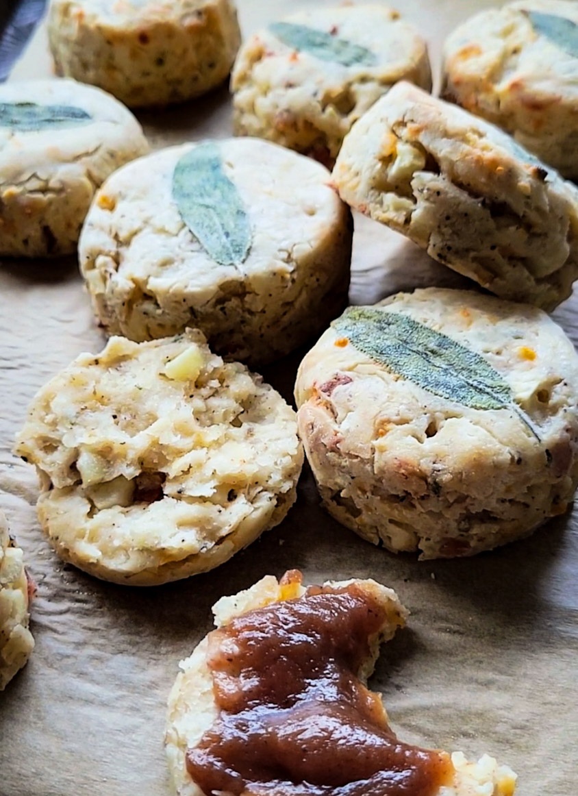 Autumn Apple, Bacon and Cheddar Biscuits with sage leaves on top, one opened and spread with apple butter.
