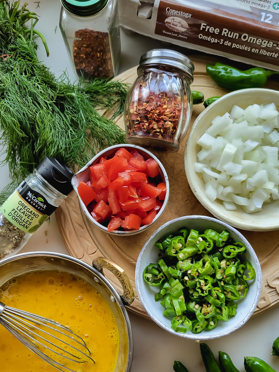 The ingredients to make Turkish Scrambled Eggs or Menemen are spread out: chopped tomatoes, onions, shishito peppers, oregano, dill, chilli flakes and eggs.