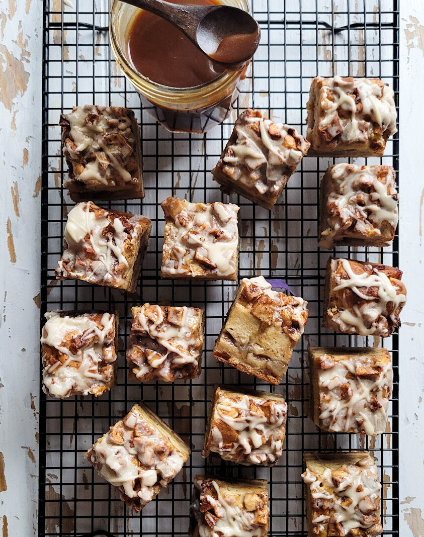Cooling rack with apple fritter squares drizzled with salted bourbon caramel glaze. A jar of salted bourbon caramel sits to the side.