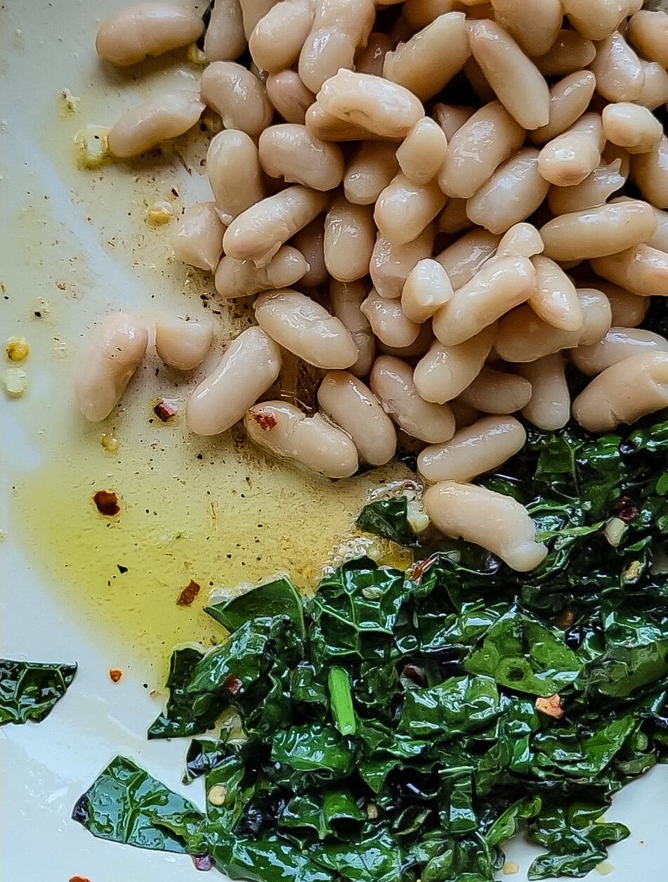 A skillet with browned butter, beans, and kale sautéing in it.