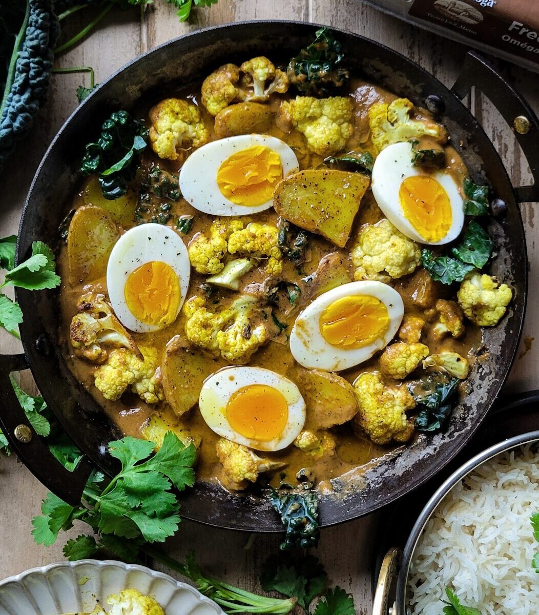 Egg, Potato and Cauliflower Curry in a skillet. Kale, and basmati rice are on the side.