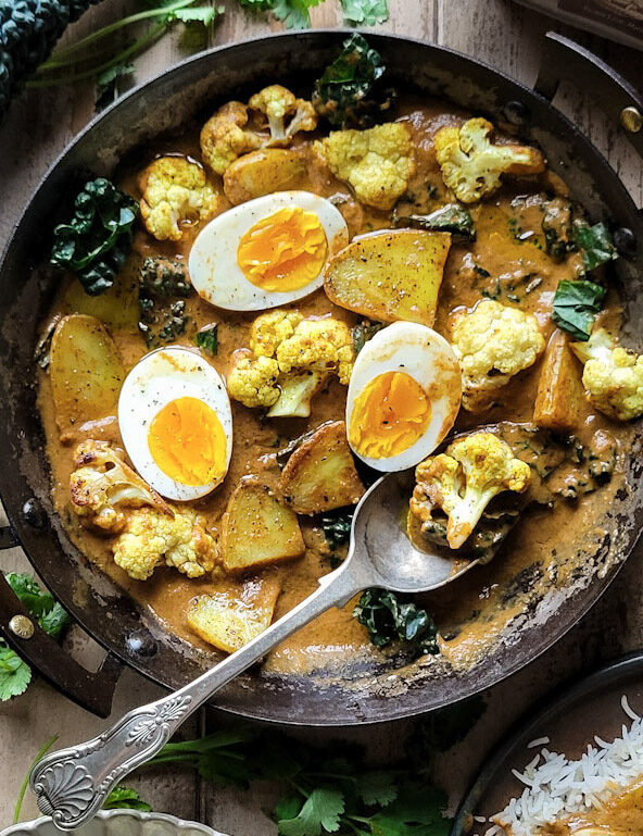 Egg, Potato and Cauliflower Curry in a skillet. Kale, and basmati rice are on the side.