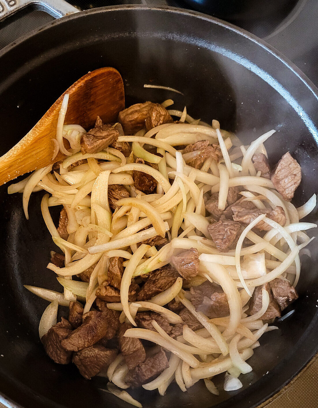 A pot is filled with sautéed beef cubes and sliced onions, to make German Goulash Soup.