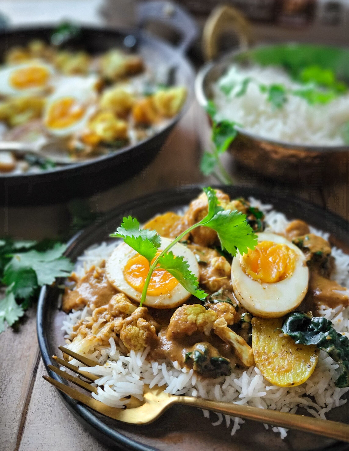 Egg, Potato and Cauliflower Curry in a skillet. Kale, and basmati rice are on the side.