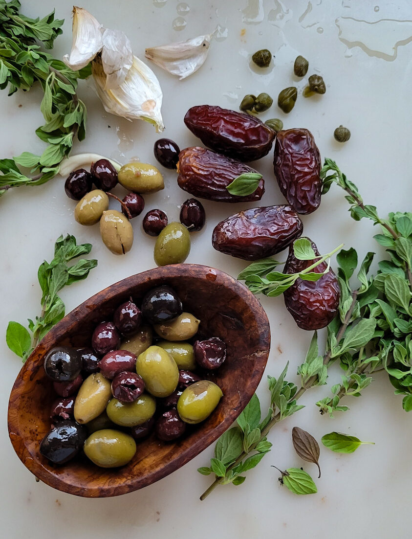 Ingredients for Roasted Cornish Game Hens Marbella: dates, garlic, oregano and olives, all spread out on the counter.