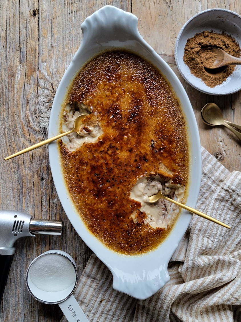Chai Eggnog Creme Brulee with two spoons cracking through the burnt sugar topping, and a kitchen torch to the side.
