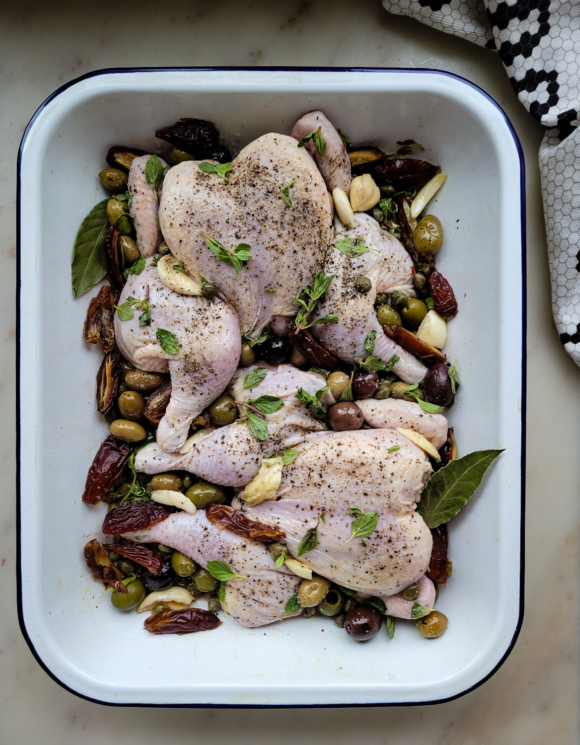 Baking dish with Cornish Game Hens, dates, olives, garlic, and oregano getting ready to be roasted in the oven, for Roasted Cornish Game Hens Marbella