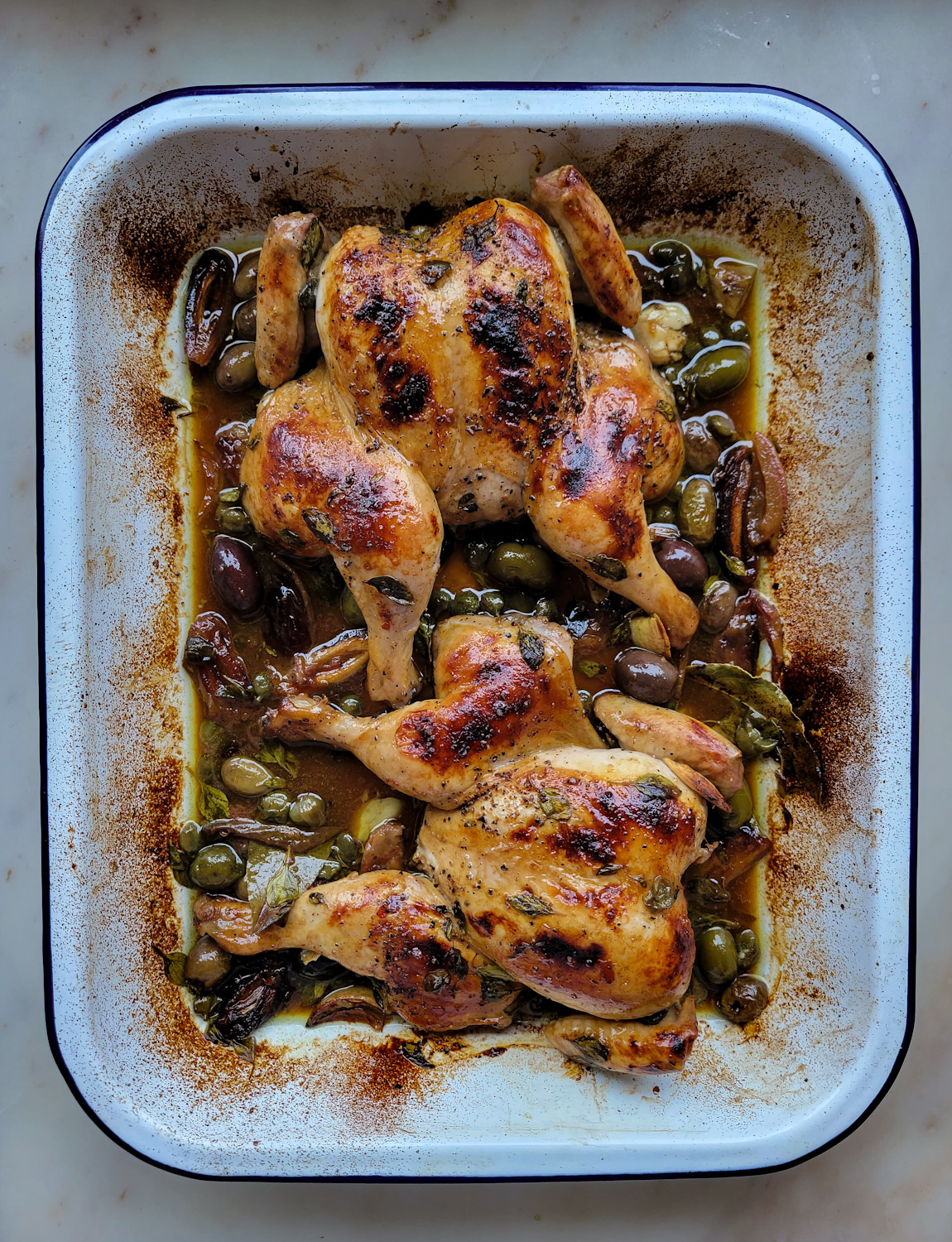 A roasting pan with Roasted Cornish Game Hen Marbella, with dates, olives, garlic and oregano.