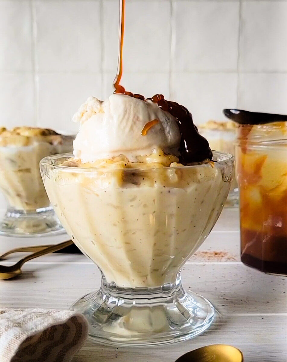 A bowl of Rice Pudding with ice cream and caramel sauce on top, a spoon to the side.