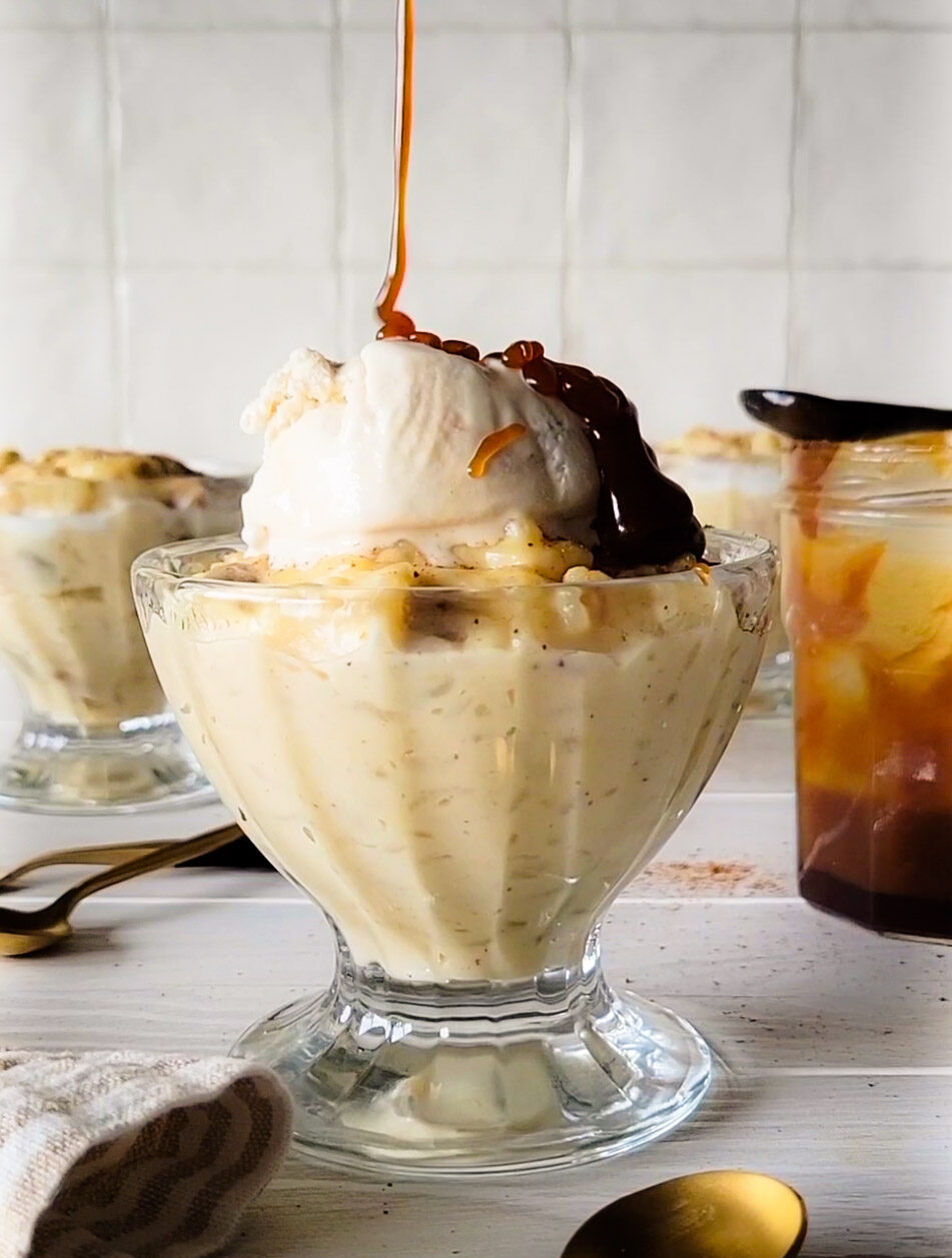 A bowl of Rice Pudding with ice cream and caramel sauce on top, a spoon to the side.