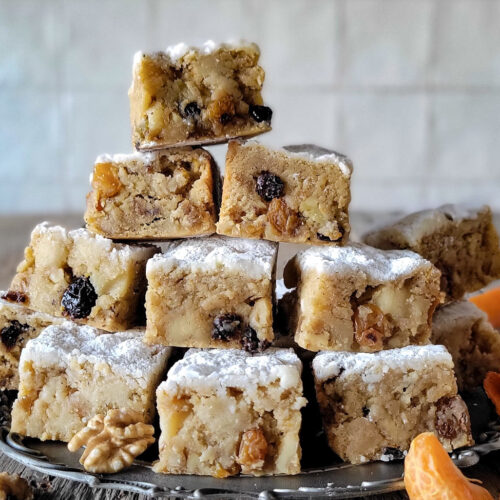 A pile of Stollen Blondies sits on a pewter plate, surrounded by walnuts and clementine segments.