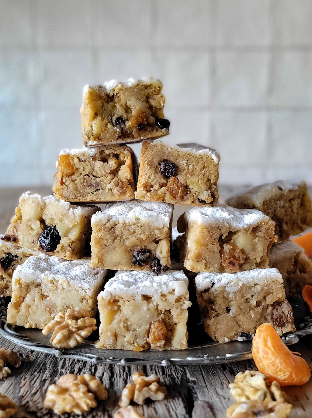 A pile of Stollen Blondies sits on a pewter plate, surrounded by walnuts and clementine segments.