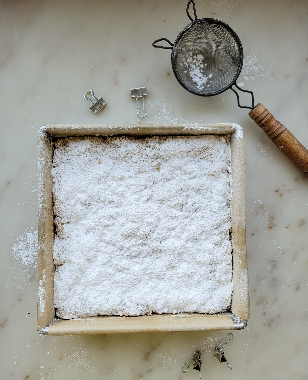 Baked Stollen Blondies in the pan, with a sifter and icing sugar beside it.