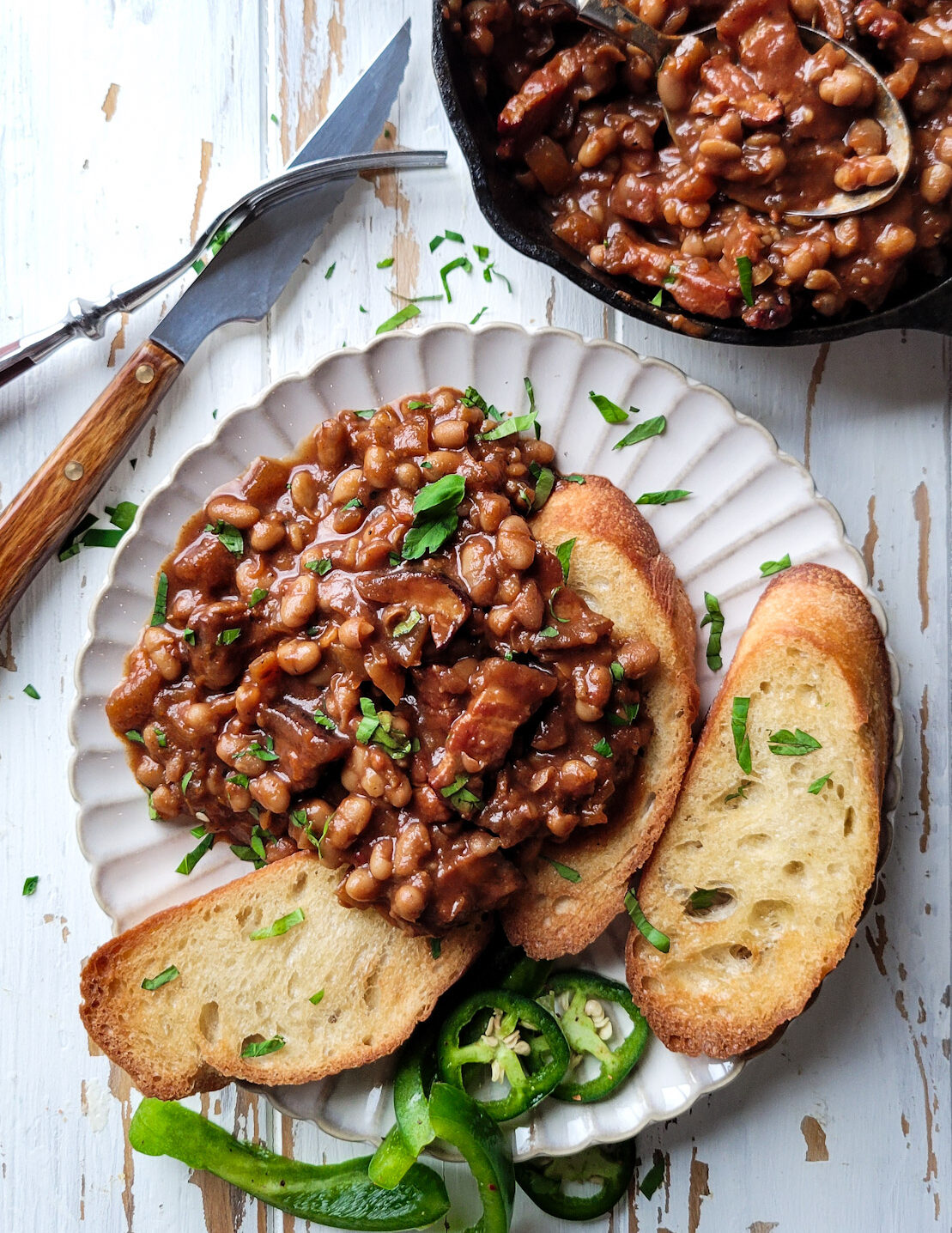 a plate with Classic Baked Beans on Toast, with the skillet of baked beans to the side. The plate is garnished with parsley and peppers.