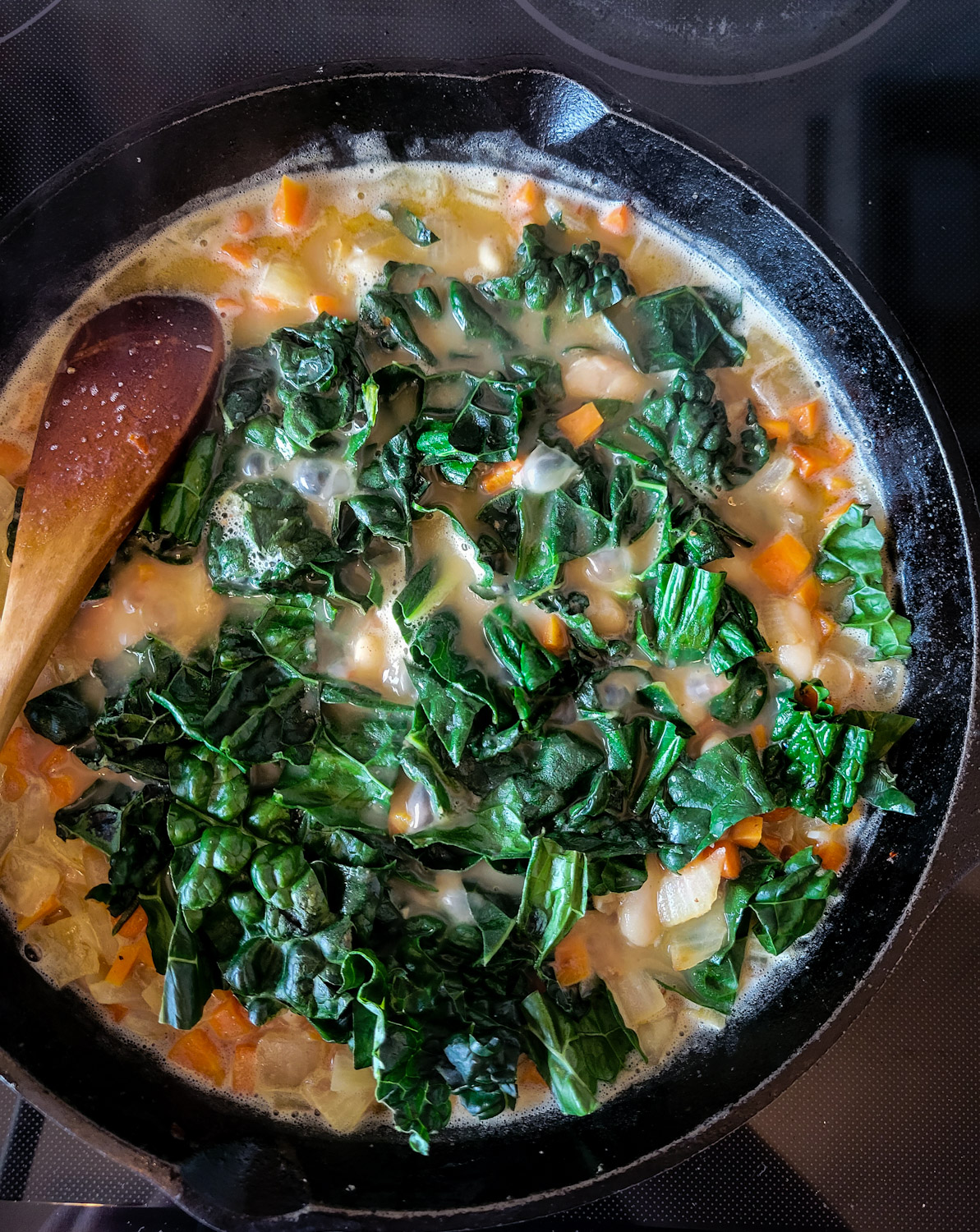A skillet of Brothy Beans with Sausage and Kale is simmering, the chopped fresh kale has just been added.