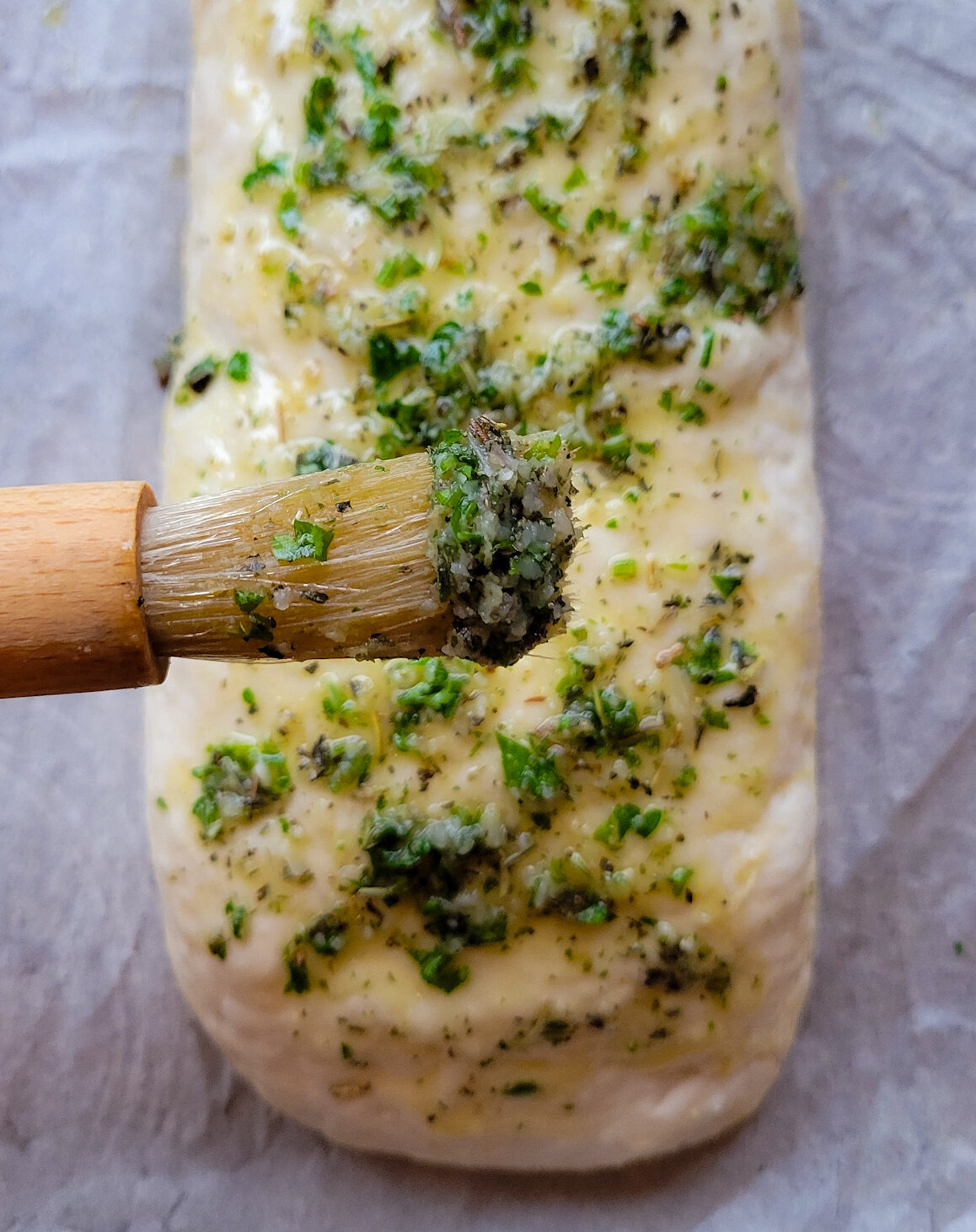 A rolled up Stromboli or pizza, being brushed with a garlic herb butter sauce.