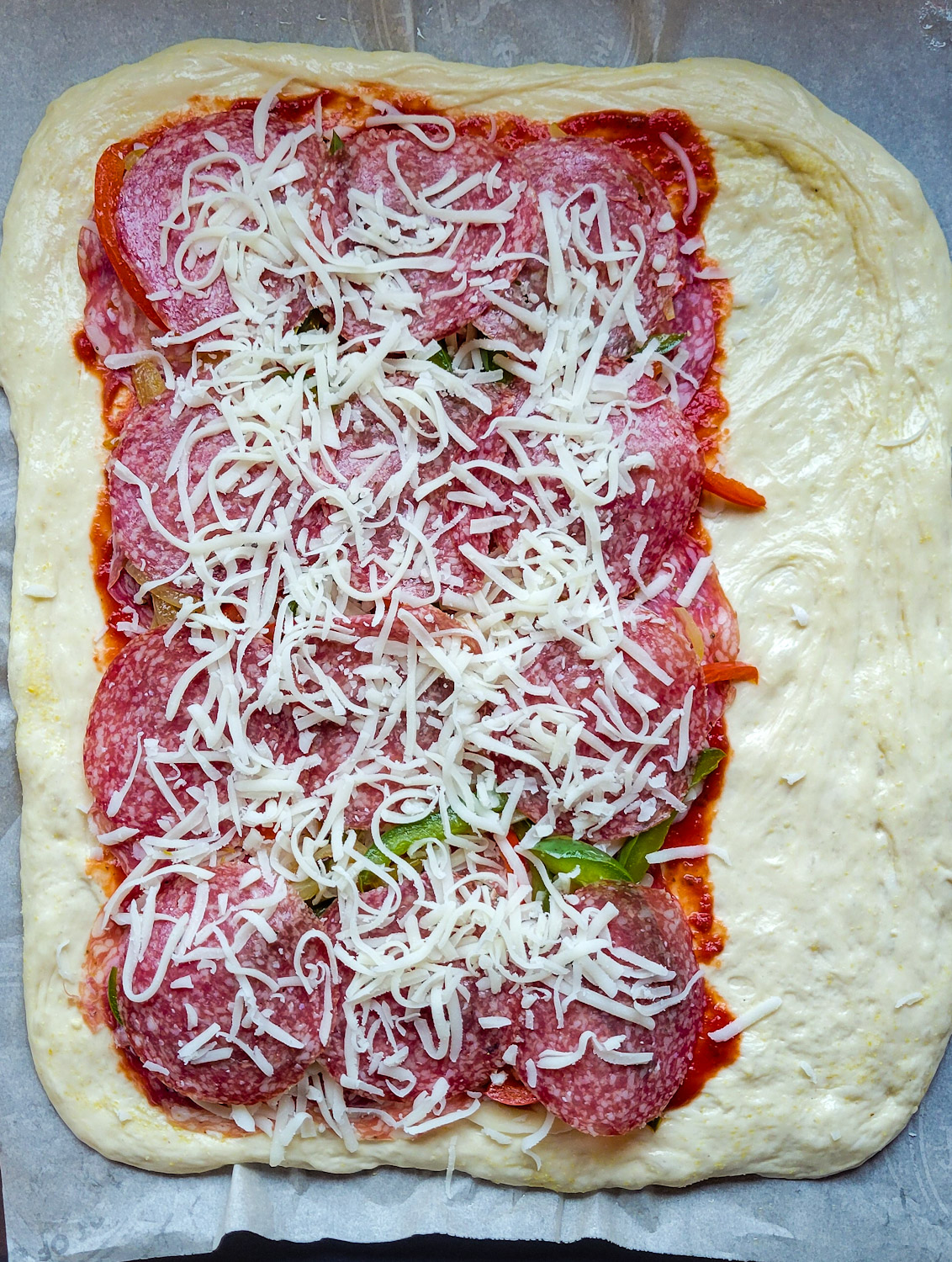 Showing all the layers of ingredients before rolling up a stromboli or rolled pizza.