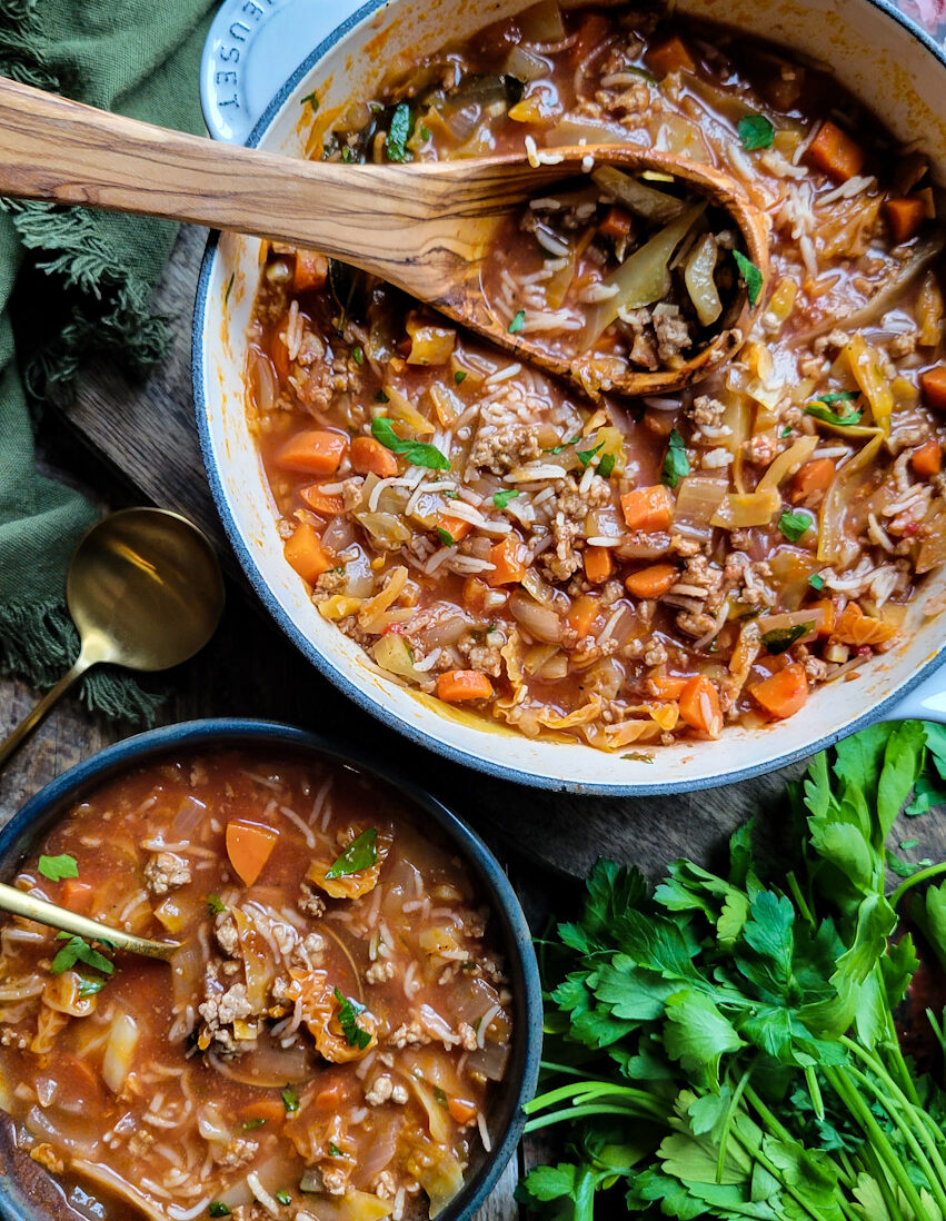 A pot of Cabbage Roll Soup with a ladle, and a bowl of the soup to the side. Parsley is on the side.