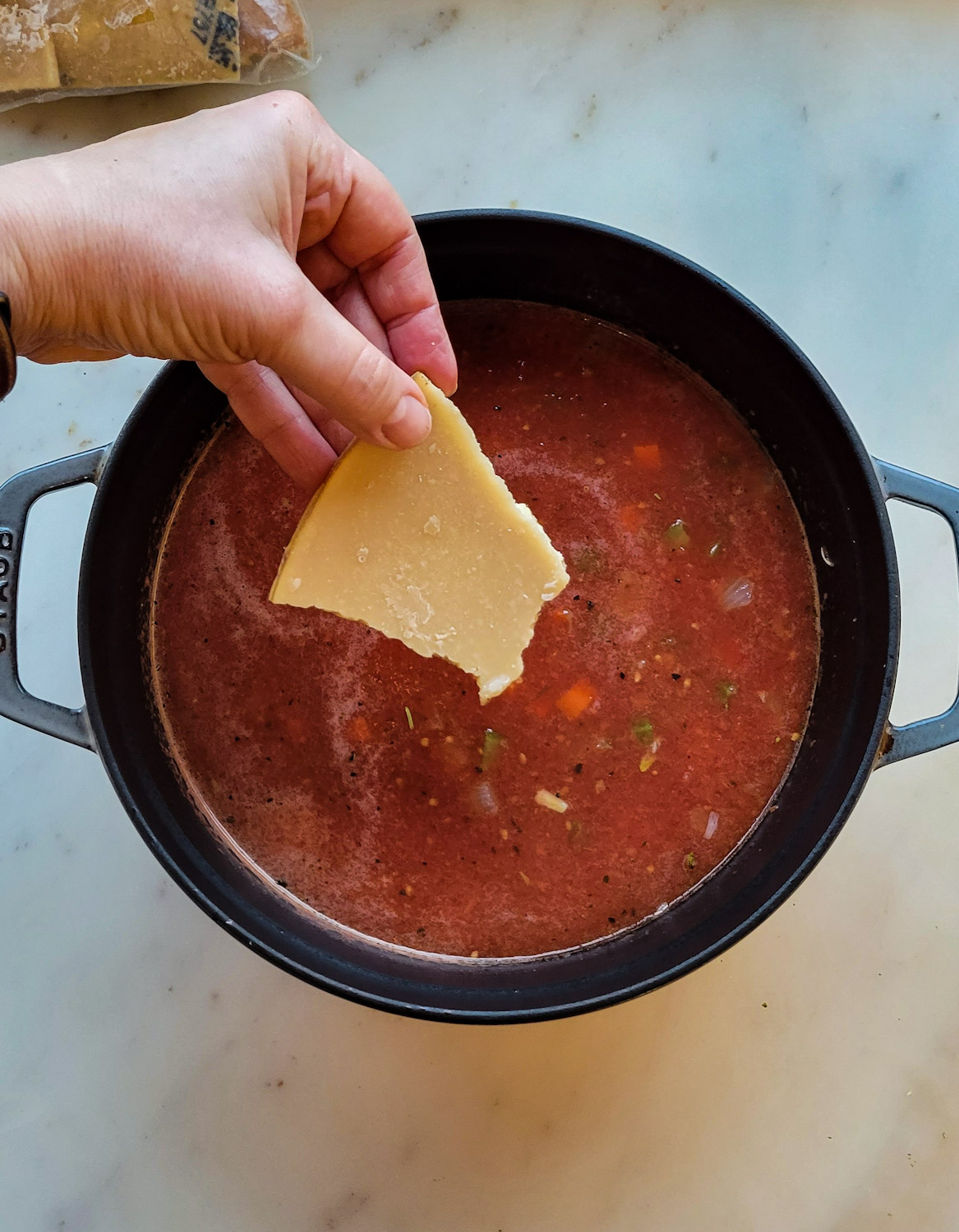 A hand adding a piece of parmesan rind to the Meatball Soup.