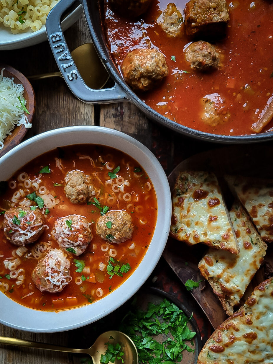A pot of meatball soup is accompanied with a bowl of the soup, as well as slices of cheesy garlic bread