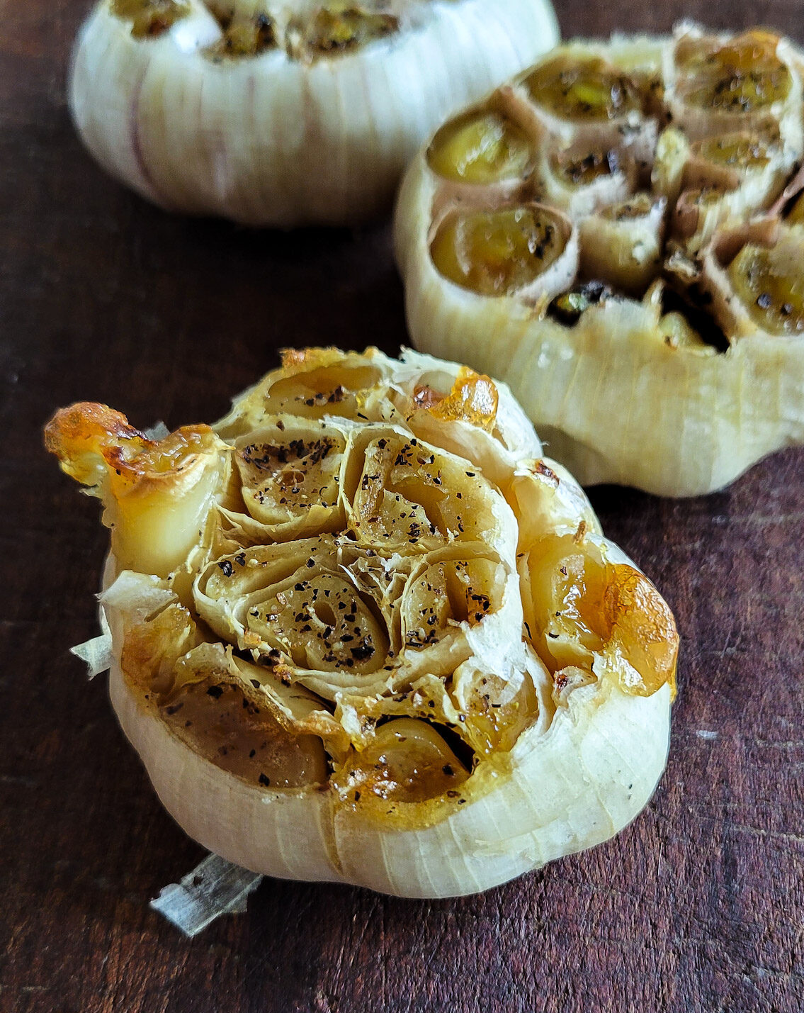 Three heads of creamy roasted garlic sitting on a cutting board.