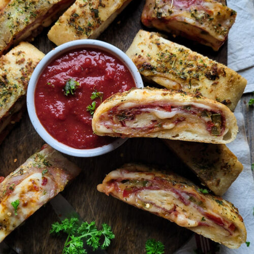 A cutting board with slices of Stromboli (rolled pizza) with harissa marinara dipping sauce.